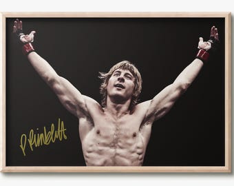May include: A framed photograph of a shirtless fighter with blonde hair, arms raised in victory, wearing black and red fingerless gloves against a black background. The image features a gold-colored signature in the lower left corner.