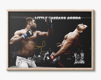 May include: A framed photograph of a UFC fight at Little Caesars Arena, showing one fighter landing a punch on another. The image is in black and white with a gold signature overlaid in the center. Both fighters wear black gloves and shorts.