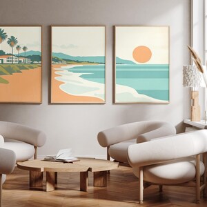 May include: A set of three vertical wall art prints featuring a coastal landscape. The artwork displays a beach scene with palm trees, a house, rolling hills, and a large orange sun over a turquoise ocean, rendered in a flat, graphic illustration style.