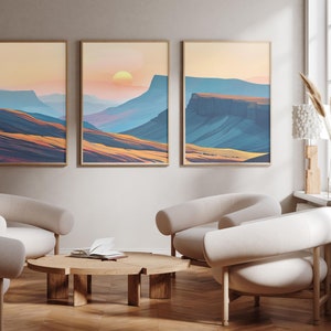 May include: Three framed landscape paintings depicting a mountain range with a sunset in the background. The paintings are hung on a pale beige wall above a wooden coffee table and three white armchairs.