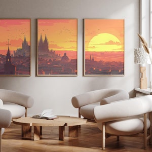 Może przedstawiać: Trzy oprawione wydruki miejskich krajobrazów o zachodzie słońca w ciepłych odcieniach pomarańczowego i żółtego. Wydruki przedstawiają panoramę miasta z dużą katedrą w centrum. Wydruki wiszą na białej ścianie w salonie z białymi fotelami i drewnianym stolikiem kawowym.