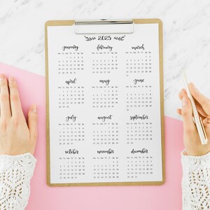 May include: A brown clipboard with a 2025 calendar printed on it. The calendar is divided into 12 months, with each month displayed in a separate box. The months are January, February, March, April, May, June, July, August, September, October, November, and December.