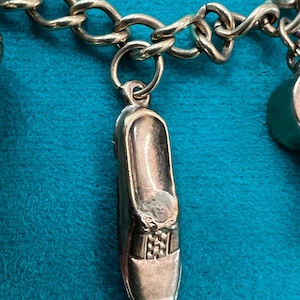 May include: A silver charm bracelet with a shoe charm. The shoe charm is detailed with a bow and a checkered pattern.