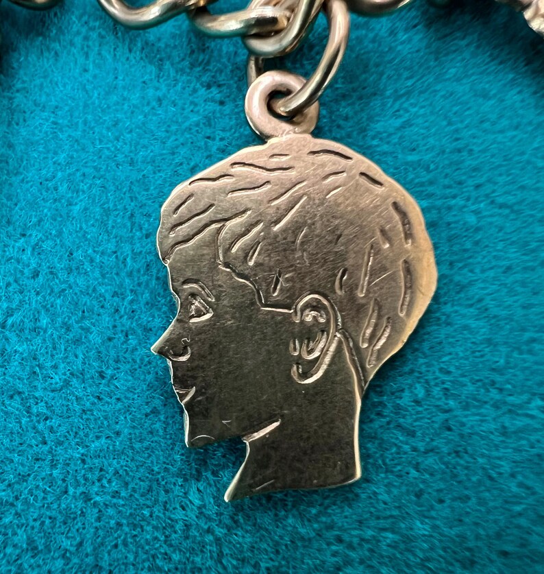 May include: A gold-toned charm in the shape of a person's head, with a side profile of a person with short hair. The charm is detailed with facial features and a textured surface.