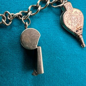 May include: A silver charm bracelet with a whistle charm and a decorative charm. The whistle charm is round with a silver finish. The decorative charm is ornate and has a silver finish.