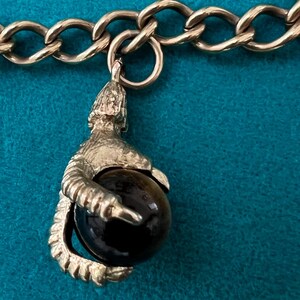 May include: A silver charm bracelet with a silver charm of a claw holding a black gemstone.