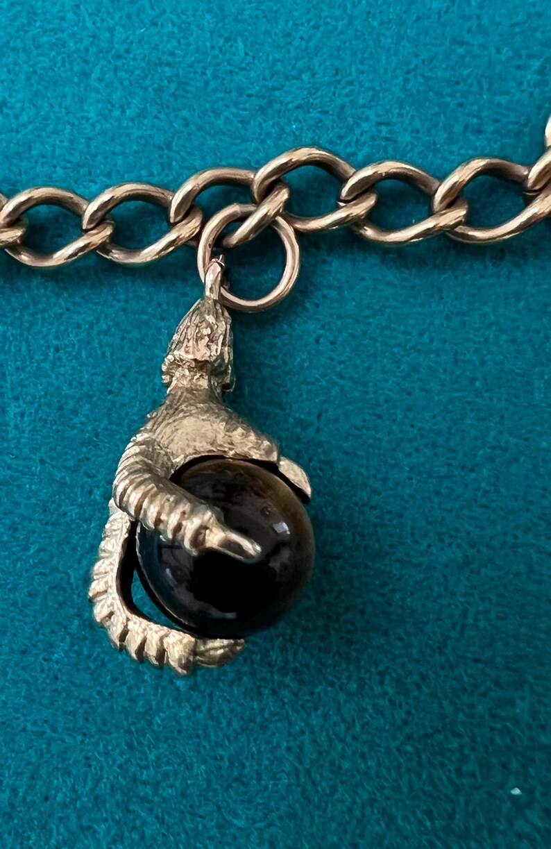 May include: A silver charm bracelet with a silver charm of a claw holding a black gemstone.
