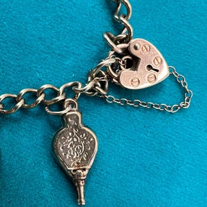 May include: A silver charm bracelet with a heart-shaped padlock charm and a silver charm shaped like a bellows.