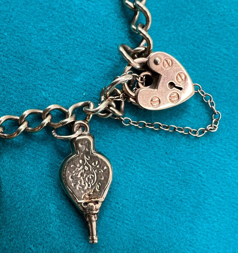 May include: A silver charm bracelet with a heart-shaped padlock charm and a silver charm shaped like a bellows.
