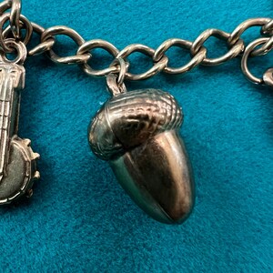 May include: A gold charm bracelet with a gold acorn charm. The acorn charm is detailed with a textured surface and a rounded shape.