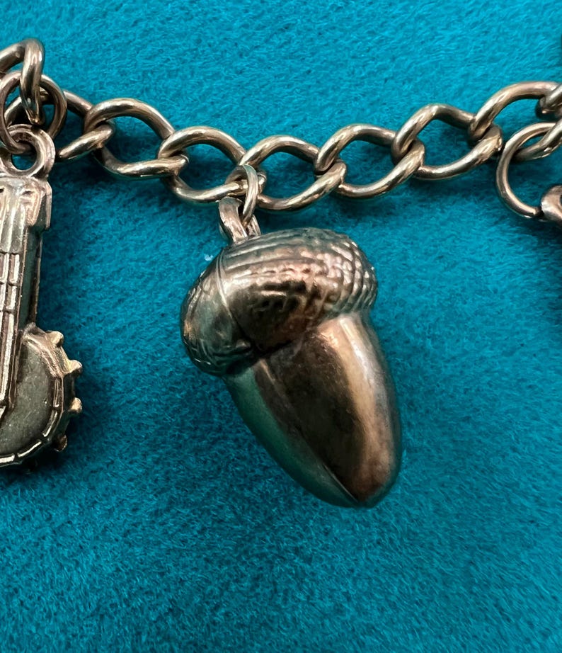 May include: A gold charm bracelet with a gold acorn charm. The acorn charm is detailed with a textured surface and a rounded shape.