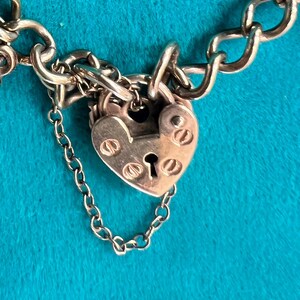 May include: A silver charm bracelet with a heart-shaped padlock charm. The padlock has a keyhole and is decorated with small, round details.