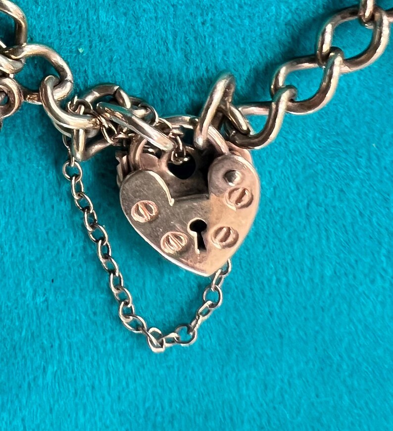 May include: A silver charm bracelet with a heart-shaped padlock charm. The padlock has a keyhole and is decorated with small, round details.