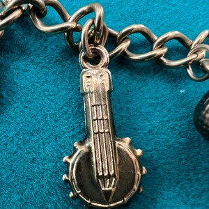 May include: Gold charm in the shape of a banjo with a detailed design. The charm is attached to a gold chain.