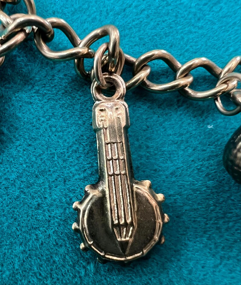 May include: Gold charm in the shape of a banjo with a detailed design. The charm is attached to a gold chain.