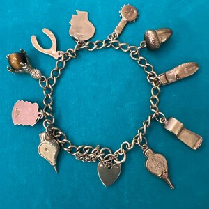 May include: A gold charm bracelet with a variety of charms, including a horseshoe, a heart, a thimble, a whistle, a cat, a  toy drum, an acorn, a  bird, and a  tiger's eye stone.