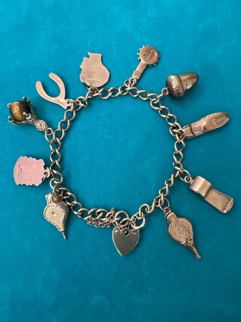 May include: A gold charm bracelet with a variety of charms, including a horseshoe, a heart, a thimble, a whistle, a cat, a  toy drum, an acorn, a  bird, and a  tiger's eye stone.
