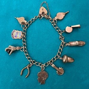 May include: A gold charm bracelet with a variety of charms, including a heart lock, a whistle, a shoe, an acorn, a horseshoe, a boy's head, a musical instrument, a bird, and a charm with the words "Old England".