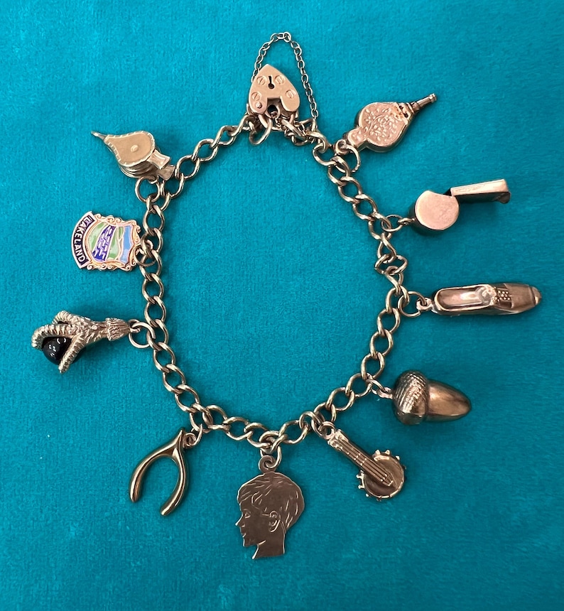 May include: A gold charm bracelet with a variety of charms, including a heart lock, a whistle, a shoe, an acorn, a horseshoe, a boy's head, a musical instrument, a bird, and a charm with the words "Old England".