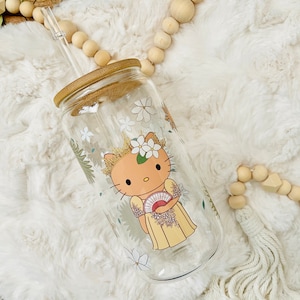 May include: A clear glass reusable water bottle with a bamboo lid and a straw. The bottle has a floral design with a cartoon cat wearing a yellow dress and holding a fan.