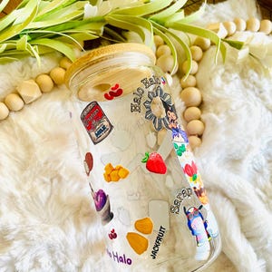 May include: A clear glass jar with a bamboo lid decorated with colorful stickers. The stickers feature images of fruit, food, and a cartoon character. The jar is labeled "Halo" and "Jackfruit".