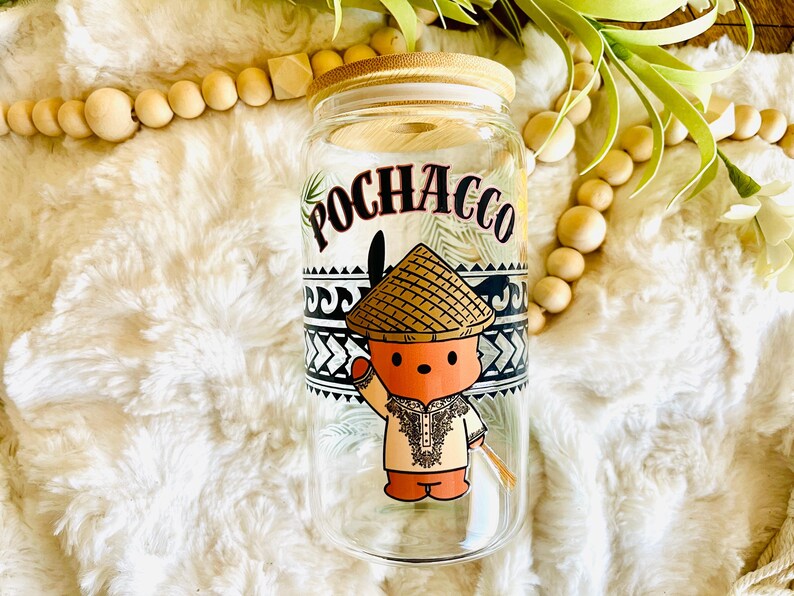 Puede incluir: Un vaso de vidrio transparente con tapa de bamb&uacute; con la palabra "POCHACCO" en escritura negra. El vaso tiene una ilustraci&oacute;n de dibujos animados de un personaje que lleva un sombrero c&oacute;nico y ropa tradicional. El dise&ntilde;o incluye patrones geom&eacute;tricos en blanco y negro.