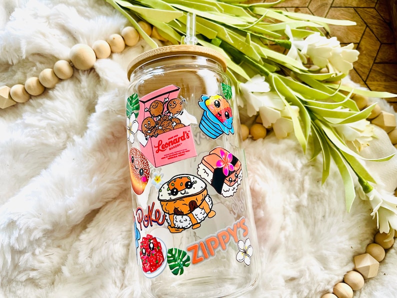 Puede incluir: Una botella de agua reutilizable de vidrio transparente con tapa de bamb&uacute; y una pajita. La botella est&aacute; decorada con pegatinas coloridas que representan comida y bebidas hawaianas, incluyendo poke, sushi, hielo raspado y donas de la panader&iacute;a Leonard's. Las pegatinas tienen caras de dibujos animados y el texto "Zippy's" y "Leonard's Bakery".
