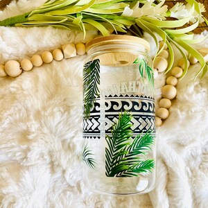 Puede incluir: Un vaso de vidrio transparente con tapa de bamb&uacute;, con un dise&ntilde;o tropical con hojas de palmera y patrones geom&eacute;tricos en blanco y negro. La palabra "MAHALO" est&aacute; impresa en el vaso. El vaso est&aacute; rodeado de elementos decorativos.