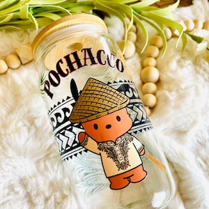 Puede incluir: Vaso de vidrio transparente con tapa y pajita de bamb&uacute;, con la palabra "POCHACCO" y un personaje de dibujos animados con sombrero de paja y ropa tradicional. El dise&ntilde;o incluye patrones tribales en blanco y negro.