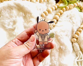May include: A clear acrylic retractable badge reel featuring a cartoon character with a beige body, black ears, and a patterned shirt. The badge reel has the word "POCHACCO" printed on it. The background is a fluffy white surface.