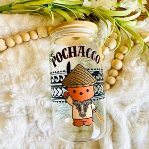 Puede incluir: Un vaso de vidrio transparente con tapa de bamb&uacute;, con un personaje de dibujos animados con sombrero de paja y ropa tradicional. La palabra "POCHACCO" est&aacute; impresa encima del personaje. El vaso est&aacute; decorado con patrones geom&eacute;tricos en blanco y negro.