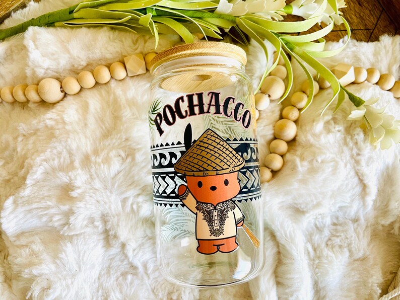 Puede incluir: Un vaso de vidrio transparente con tapa de bamb&uacute;, con un personaje de dibujos animados con sombrero de paja y ropa tradicional. La palabra "POCHACCO" est&aacute; impresa encima del personaje. El vaso est&aacute; decorado con patrones geom&eacute;tricos en blanco y negro.