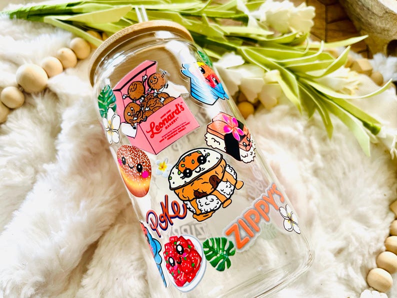 Puede incluir: Una botella de agua reutilizable de vidrio transparente con tapa de bamb&uacute; y una pajita. La botella est&aacute; decorada con pegatinas coloridas que representan comida hawaiana, flores y las palabras "Poke" y "Zippy's".