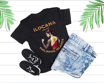 May include: Black t-shirt with a graphic of a woman with a tattoo of the Philippine flag. The text "ILOCANA STRENGTH PHILIPPINE ISLANDS" is printed on the shirt.