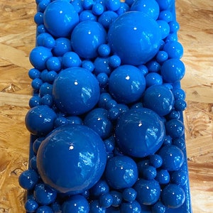 May include: A rectangular art piece featuring a vibrant arrangement of glossy, deep blue spheres of varying sizes. The spheres are densely packed, creating a textured, three-dimensional effect. The artwork is set against a dark blue background.