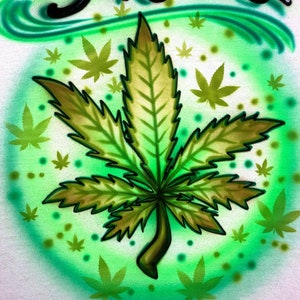 Könnte beinhalten: Ein grünes Marihuana-Blatt auf einem grün-weißen Hintergrund. Das Wort "Skelles" ist in Schwarz über dem Blatt geschrieben.