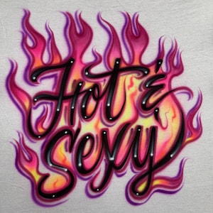 May include: Airbrushed design featuring the words "Hot & Sexy" in black script, outlined with white dots. The text is surrounded by flames in shades of pink, orange, and yellow, set against a white background.