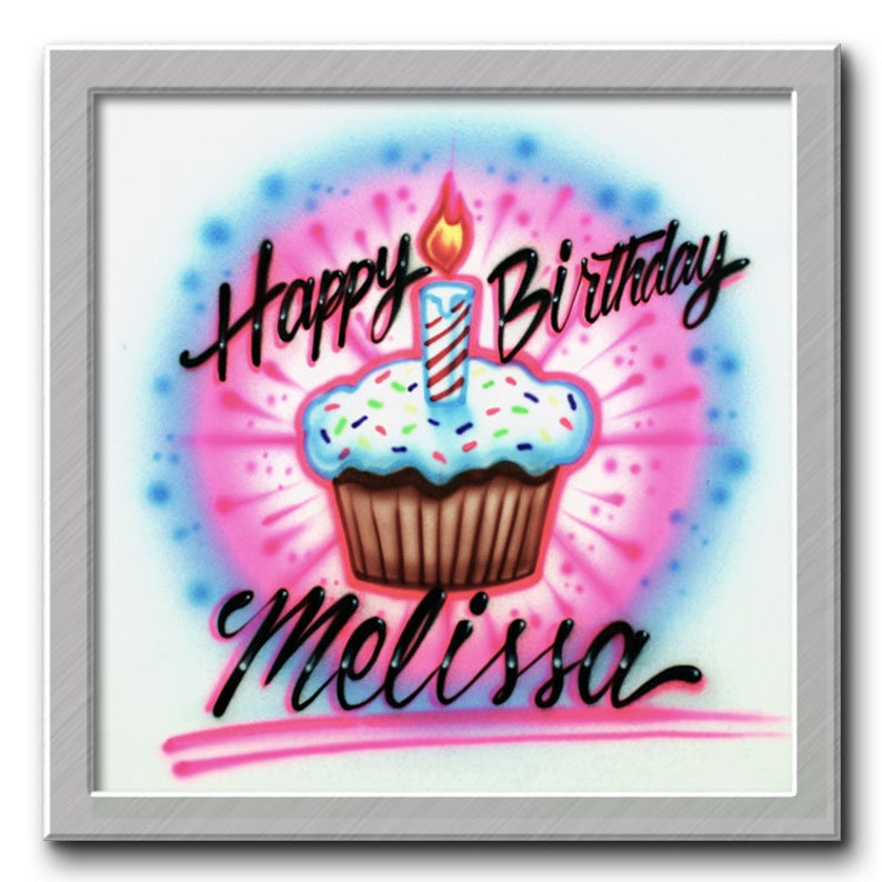 May include: A white background with a pink and blue spray paint design. In the center is a cupcake with a lit candle and sprinkles. The text "Happy Birthday Melissa" is written in black cursive.