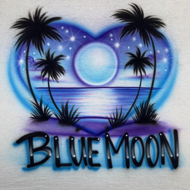 Puede incluir: Una camiseta blanca con un dise&ntilde;o en forma de coraz&oacute;n con degradados azules y morados. El dise&ntilde;o incluye palmeras, una luna llena y el texto "BLUE MOON" en negro, creando una escena nocturna tropical.