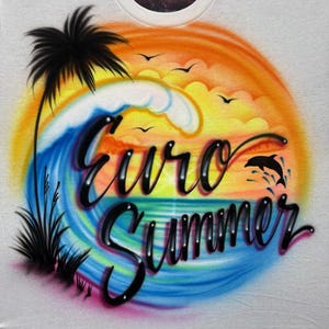 May include: White t-shirt with a colorful airbrushed design. The design features a sunset, ocean waves, a palm tree, and the words "Euro Summer" in a glossy black font. A dolphin is jumping out of the water.