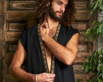 May include: Black sleeveless top with a decorative gold and brown geometric pattern along the edges. The top is made of a textured fabric and is worn open. The background is a wooden door and green foliage.