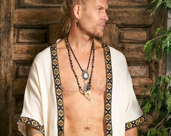 May include: A white linen kimono with black and gold trim. The kimono has a relaxed fit and is open in the front. The model is wearing a black belt with gold accents and several necklaces.