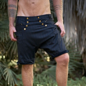 May include: A person wearing black and white striped shorts with gold buttons. The shorts have a unique, loose fit and are worn with bare legs.