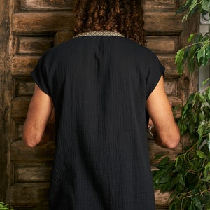 Pode incluir: Uma camisa preta de manga curta com uma borda dourada em volta do decote. A camisa &eacute; feita de um tecido macio e texturizado.