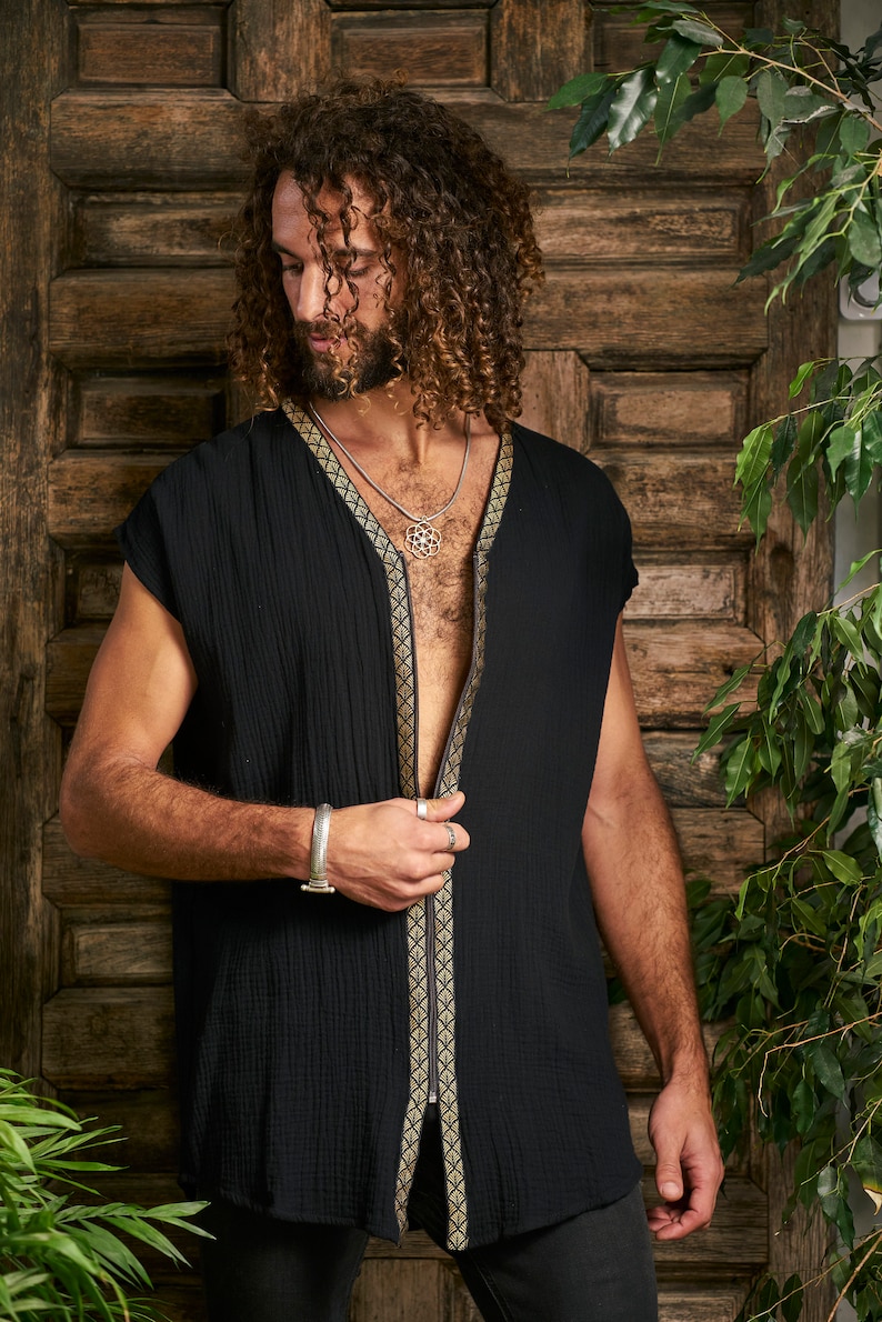 Pode incluir: Uma camisa preta sem mangas com fecho de z&iacute;per e guarni&ccedil;&otilde;es douradas. A camisa tem um padr&atilde;o geom&eacute;trico nas guarni&ccedil;&otilde;es. O modelo est&aacute; usando um colar de prata com um pingente geom&eacute;trico.