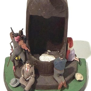 May include: A dark brown, arched, hollow structure sits on a green base. A red-skinned horned figure plays a violin, a person in a tan suit sits nearby, a person in a blue shirt kneels, and a person with red hair sits on the right side.