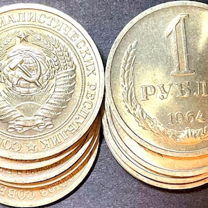 May include: Two stacks of gold-colored coins. The left stack shows the Soviet Union emblem with a hammer and sickle. The right stack shows the number 1, the Cyrillic text "РУБЛЬ", and the year 1964, all framed by two wheat stalks.
