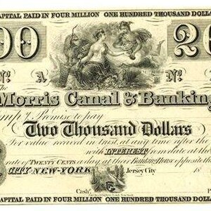 Peut inclure: Un billet de banque vintage de deux mille dollars de la Morris Canal & Banking Company en encre crème et noire. Le billet présente le texte '2000', 'Two Thousand Dollars' et 'New York', avec une illustration allégorique et des motifs complexes.