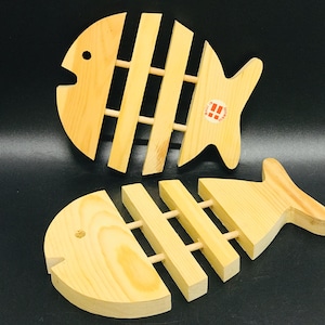 Può includere: Due sottopentola in legno a forma di pesce con un design a lamelle. I sottopentola sono in legno marrone chiaro e hanno una finitura naturale.