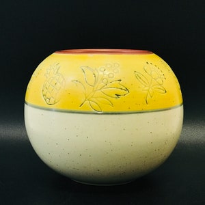Può includere: Un vaso rotondo in ceramica giallo e bianco con un disegno di ananas e foglie intorno alla parte superiore.